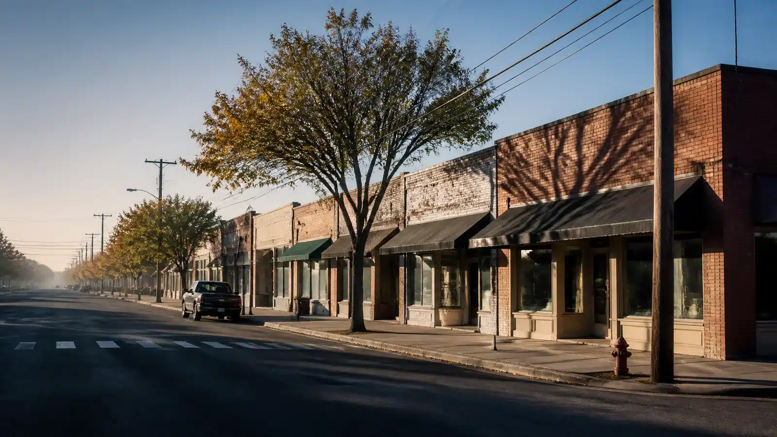 Illustrative small-town main street in the United States with low storefronts and a parked pickup truck