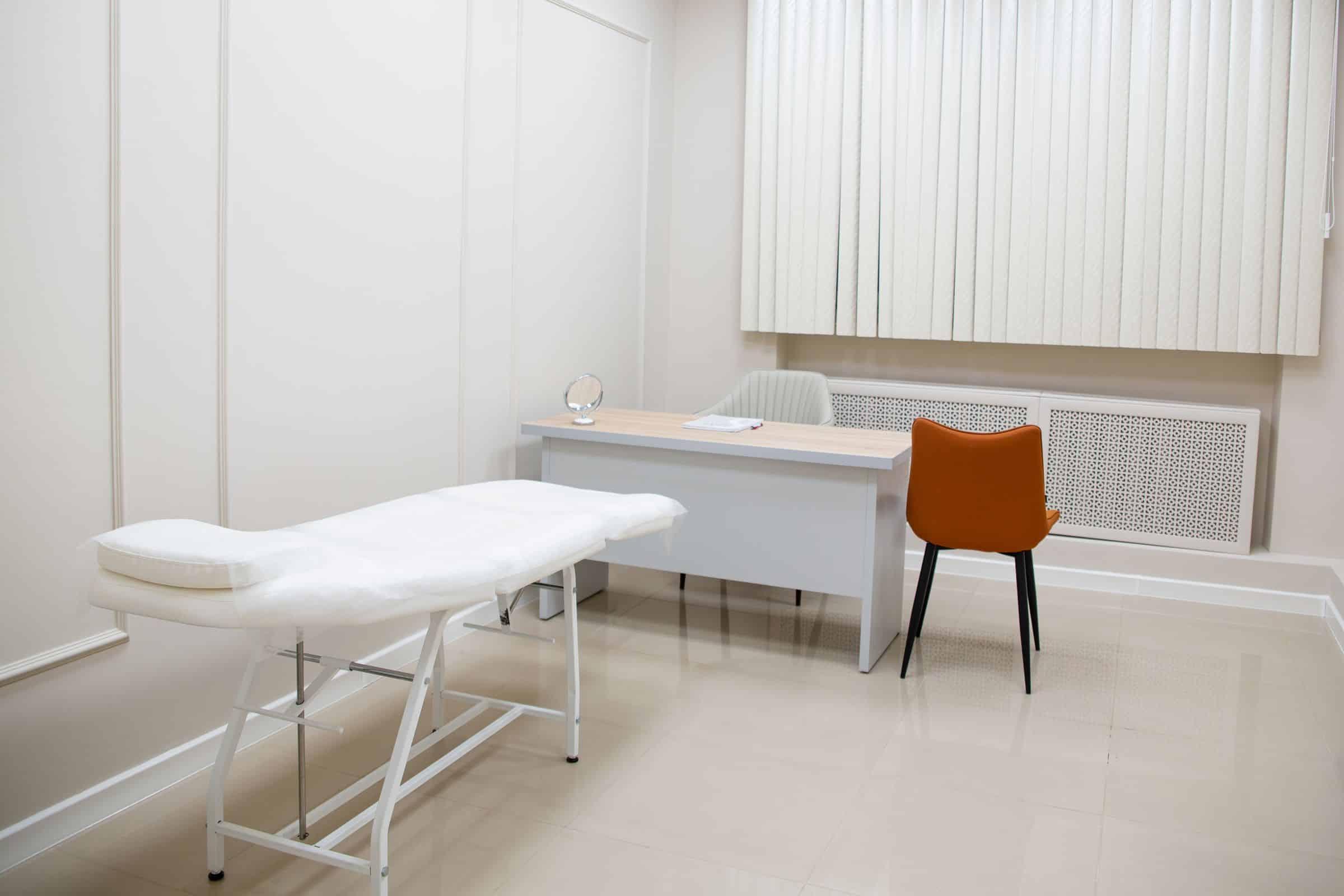 An unoccupied treatment room with white walls, a couch and a desk. Illustrative only; not a named partner hospital.
