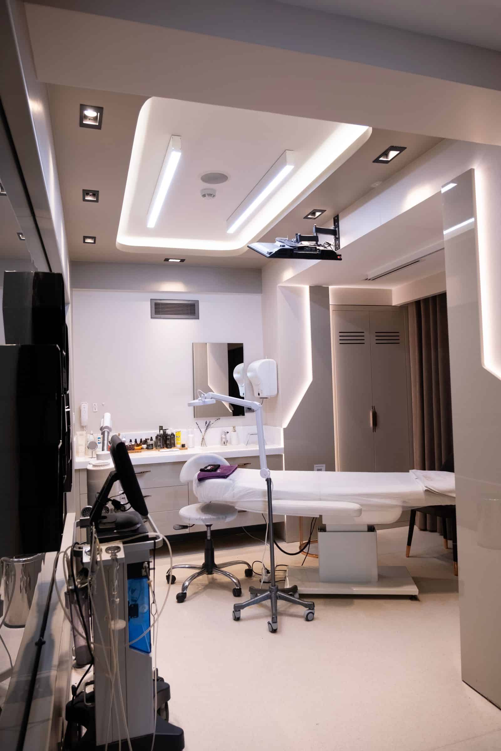 An unoccupied private clinic treatment suite with cove lighting and a treatment bed. Illustrative only.